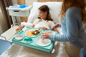 Girl lies on a hospital bed and has breakfast