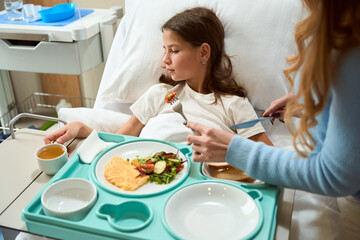 Mom helps her daughter in a hospital bed with a meal