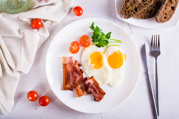 Fried eggs and bacon, tomatoes and parsley on a plate on the table. Homemade breakfast. Top view
