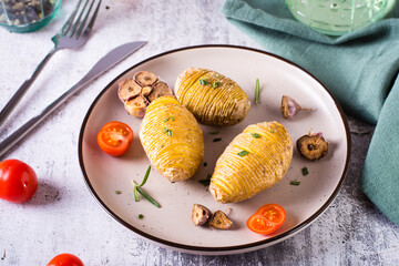 Baked hasselback potatoes with garlic and rosemary on a plate. Homemade lunch.