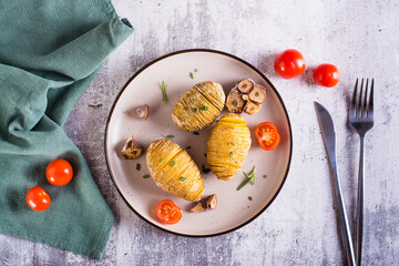Delicious homemade baked hasselback potatoes with garlic and rosemary on a plate. Top view