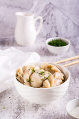 Boiled dumplings in a bowl, sour cream and greens on the table. Home made food. Vertical view