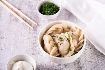 Fresh meat dumplings in a bowl with sour cream and herbs on the table. Homemade food.