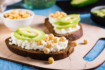 Sandwiches on rye bread with ricotta, avocado and chickpeas on a board. Healthy food.