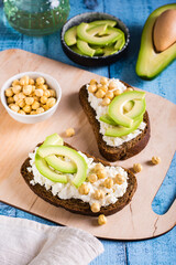 Bruschetta with ricotta, avocado and chickpeas on rye toast on a board. Healthy food. Vertical view
