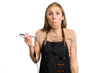 Young caucasian manicurist woman holding an electric file drill isolated shrugs shoulders and open eyes confused.