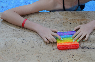 Hands play with a multicolored anti-stress toy in the form of a rainbow on an abstract background. pop it. A popular game among children and teenagers.