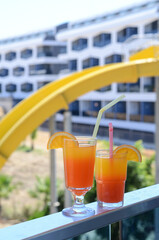 Freshly prepared delicious cocktails with straws and orange slices on the balcony against the backdrop of the water slides and the hotel building