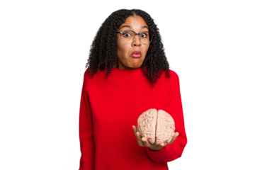 Young african american woman holding a brain model isolated shrugs shoulders and open eyes confused.