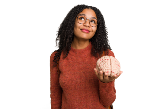 Young student african american woman holding a brain isolated dreaming of achieving goals and purposes