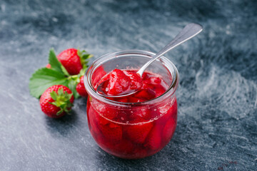 Ripe red strawberries from organic cultivation and marmalade offered as a close-up on a gray board with copy space