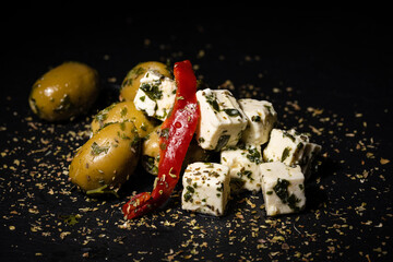 Fototapeta na wymiar olives and feta with herbs and oil on black background