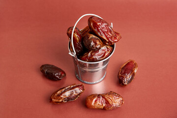 A small metal bucket filled with dried dates on a brown background.