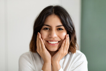 Headshot of happy attractive arabic lady touching her cheeks