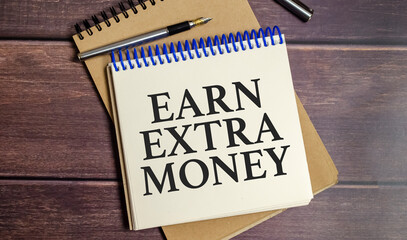 Earn extra money text on white notebook and wooden background