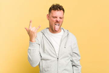 Young caucasian handsome man isolated on yellow background showing rock gesture with fingers