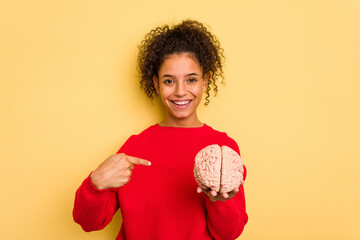 Young brazilian woman holding a brain model isolated person pointing by hand to a shirt copy space, proud and confident - obrazy, fototapety, plakaty