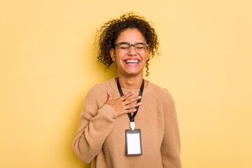 Young brazilian woman with a badge isolated on yellow background laughs out loudly keeping hand on...