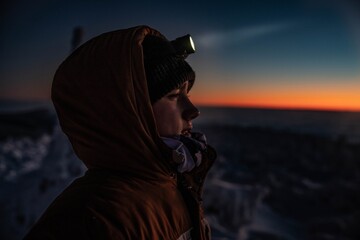 Fototapeta Teenager boy in a warm winter jacket with a headlamp on a mountain winter trail. Minutes before sunset, Babia Gora, Beskids, Poland obraz