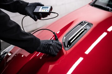 Employee of a car service checks the thickness of the paint coating of a red car