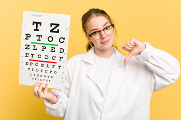 Young caucasian oculist woman holding a eye chart paper isolated on yellow background feels proud and self confident, example to follow.