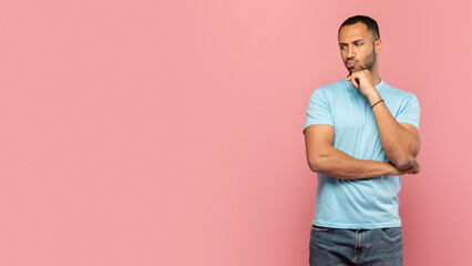 Pensive black man touching his chin, thinking and looking aside at free space on pink studio background, panorama