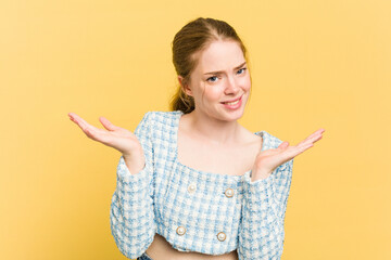 Young caucasian redhead woman isolated on yellow background doubting and shrugging shoulders in questioning gesture.