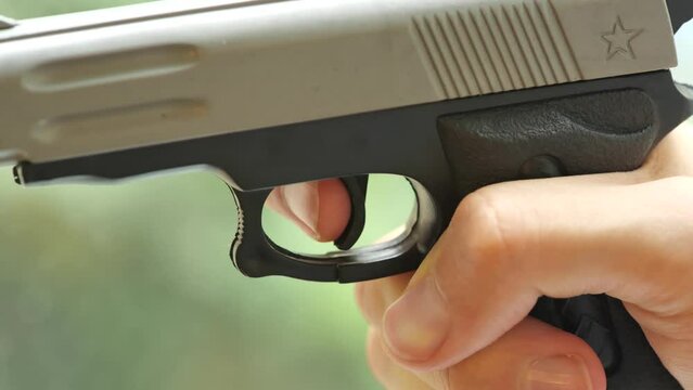 Man with shaky hands slowly pulling the trigger on a small cheap toy gun, object detail, closeup. Shooting a weapon, nervous shooter, gun safety laws rules, danger abstract concept, one person