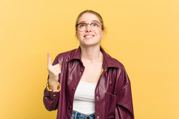 Young caucasian redhead woman isolated on yellow background indicates with both fore fingers up...