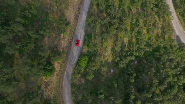 drone bird's eye view of red car driving on forest road