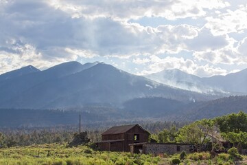 Fototapeta na wymiar Smoke rising in the mountains in the Schultz Fire near Flagstaff, Arizona. An old structure is in the foreground.