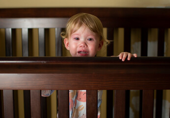 Caucasian baby girl crying in the crib. Sad Sick child
