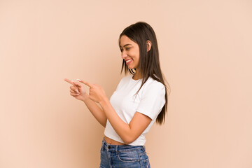 Young colombian woman isolated on beige background points with thumb finger away, laughing and...