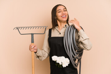 Young colombian gardener woman holding a hose isolated on beige background