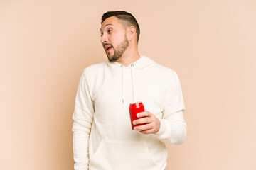 Young latin man holding a cola refreshment isolated looks aside smiling, cheerful and pleasant.