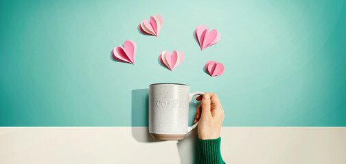 Female hand holding a mug with paper craft hearts - flat lay