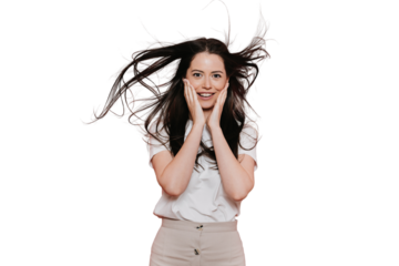 Excited brunette Italian young woman with fluttering hair in casual touching cheeks by hands in surprise stands over transparent background. Gorgeous Caucasian girl amazed by discount, sale. Mockup.