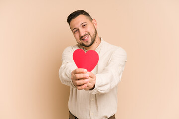 Adult latin man holding a paper heart, valentines day concept isolated