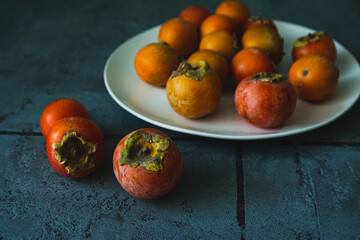 Small persimmon fruits on a white plate on a dark gray background.