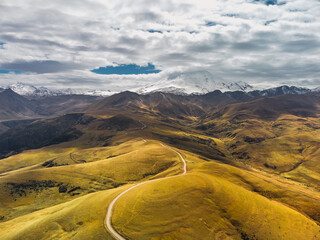 Mountain peaks covered with snow at the top and dry grass below and with clouds descending on the...