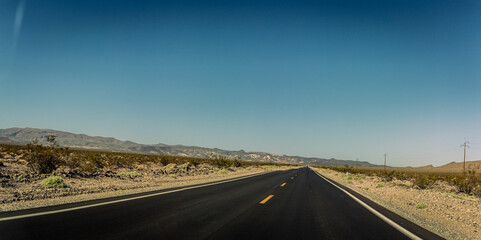 Straight road in small desert plants and sand with mountains in america at sunny day