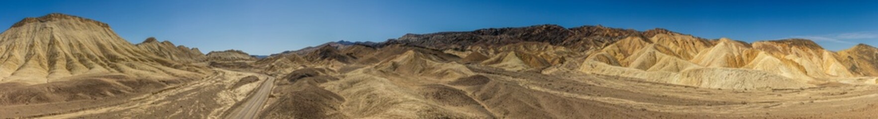 Unpaved sandy road between desert colorful mountains in Death Valley at sunny day