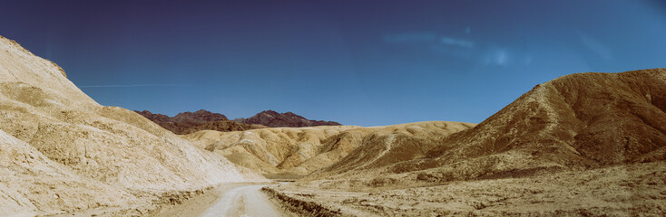 Unpaved sandy road between desert colorful mountains in Death Valley at sunny day