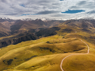 Mountain peaks covered with snow at the top and dry grass below and with clouds descending on the...