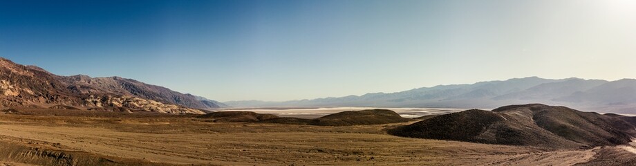Sandy desert plain with rocky mountains witout life in Death Valley at sunny day, america