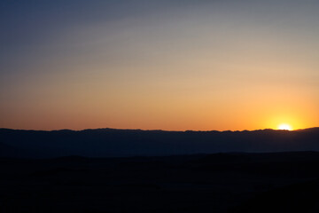 Fototapeta na wymiar Dark horizon with orange sun glare at sunset in Death Valley national park in america