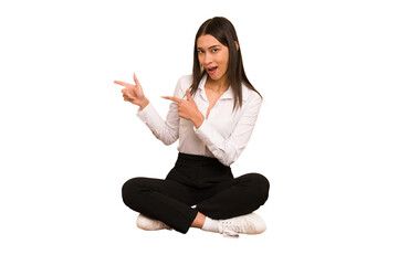 Young colombian woman sitting on the floor isolated shocked pointing with index fingers to a copy space.