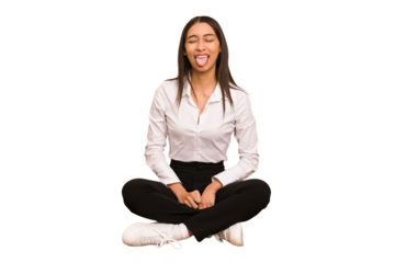 Young colombian woman sitting on the floor isolated funny and friendly sticking out tongue.