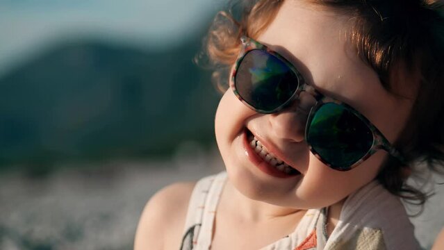 Adorable little baby wearing big sunglasses smiles at the camera, close-up