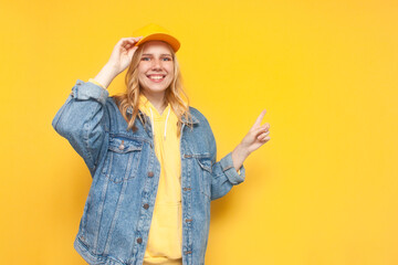girl in denim jacket and cap shows with her hand on copy space, hipster girl advertises place for text